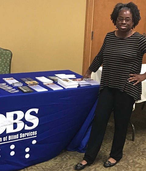DBS staff member Bertha Hyche standing next to the DBS exhibit table at the health fair. 